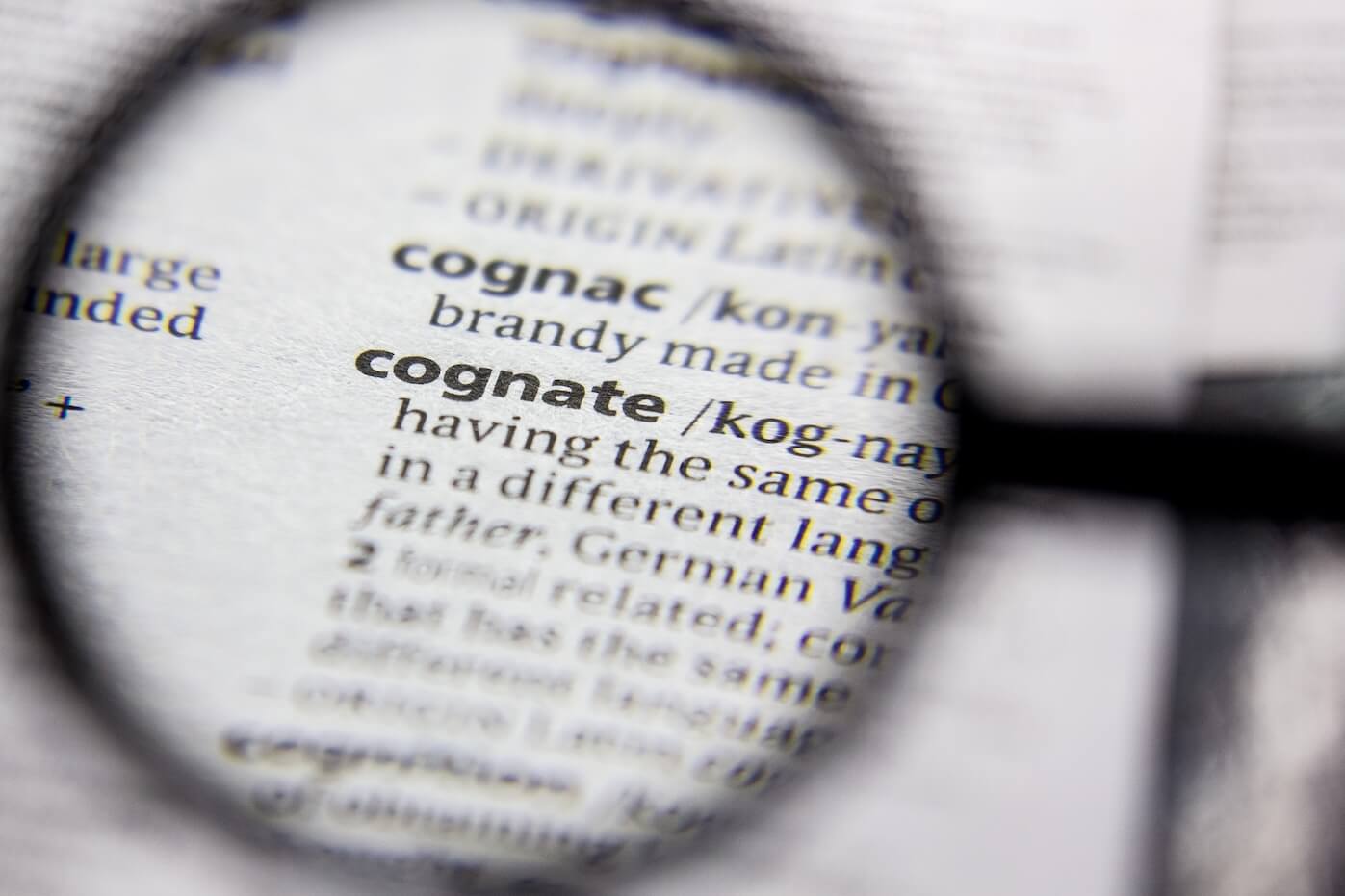 Magnifying glass zooming into a dictionary focusing on cognate word.