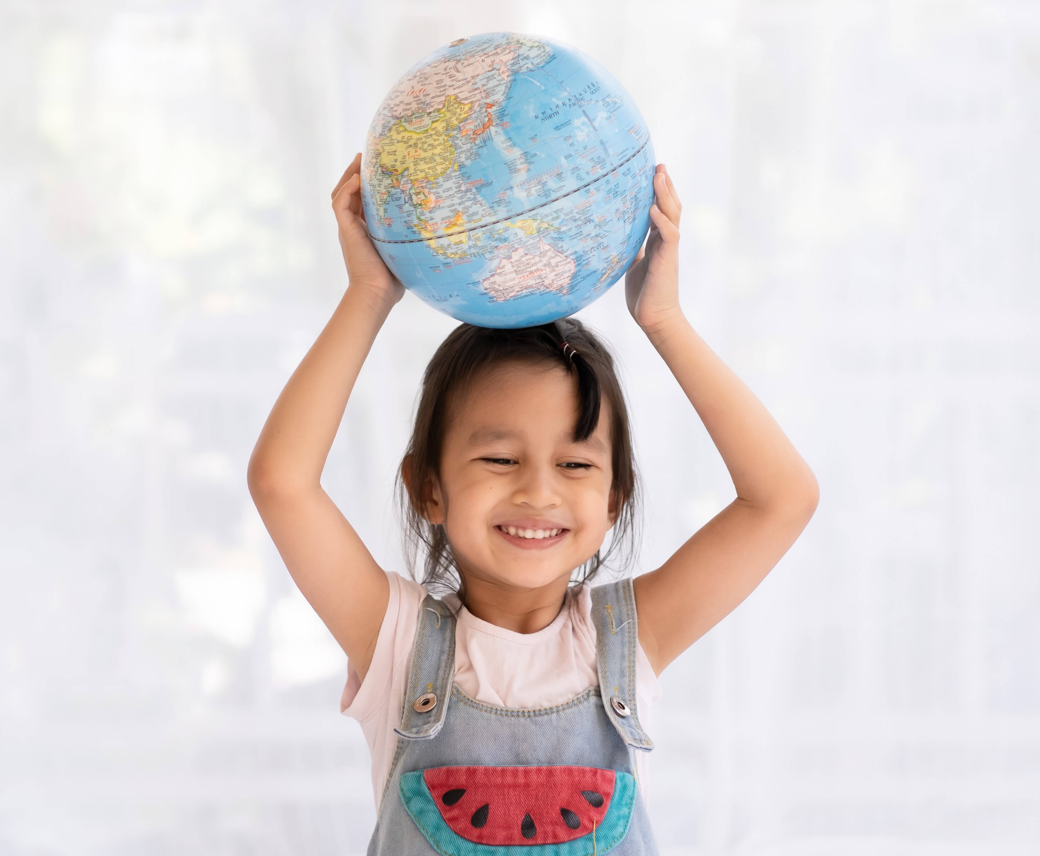 Small girl holding a globe above her hard while smiling.
