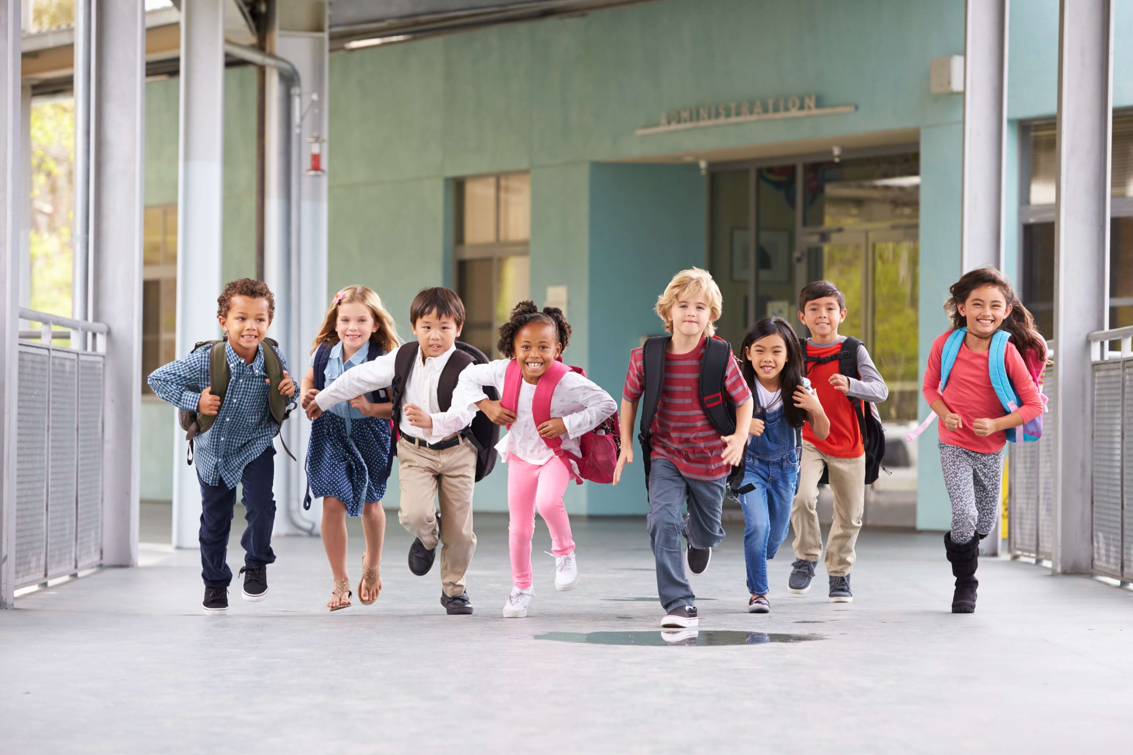 Group of small school kids running in a corridor with their backpacks on.