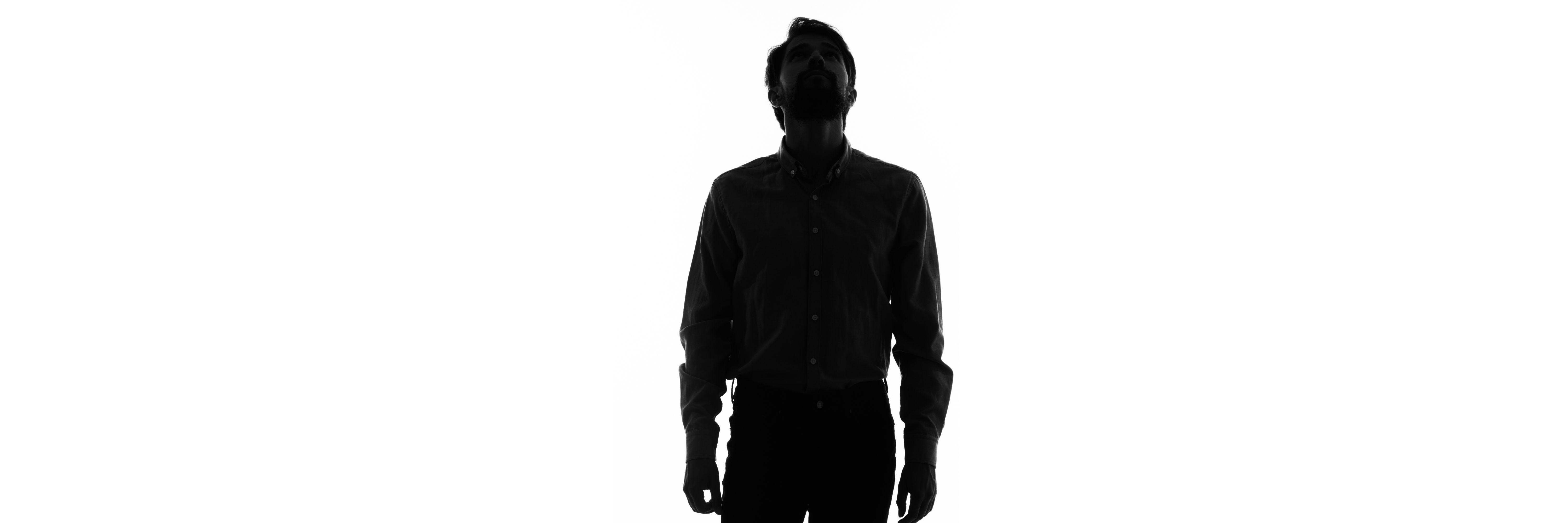 Silhouette of a person standing and looking upwards in a light background, wide