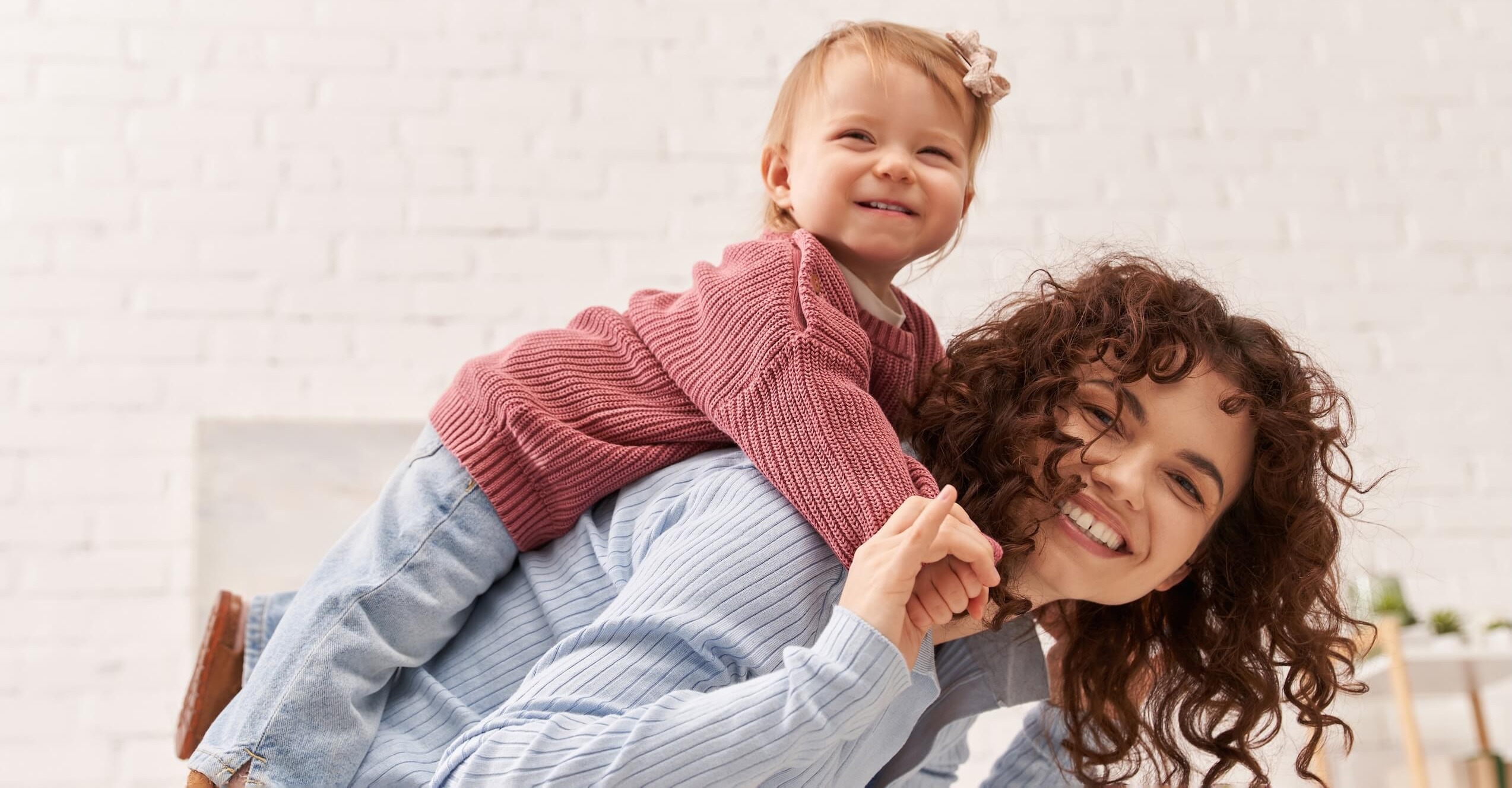 Woman is having her baby seated on her back while both laughing.