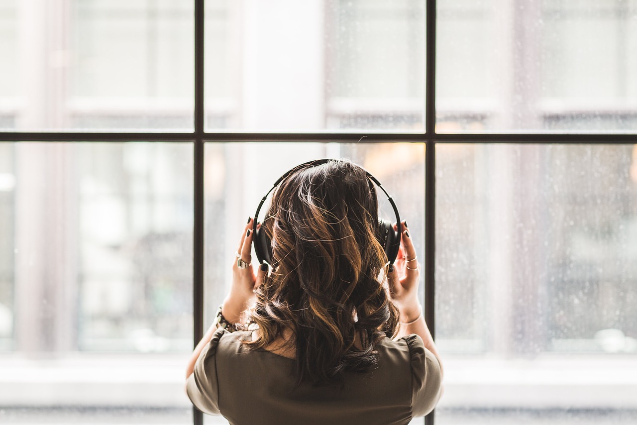 Woman listening to audiobook through headphones in front of a window.